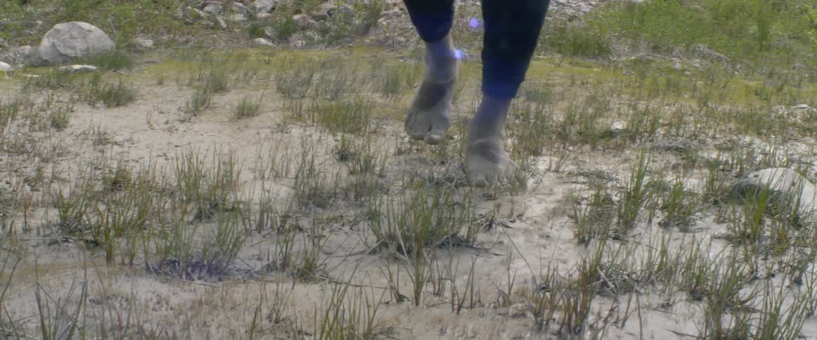 A person is walking on the grass and sand barefoot