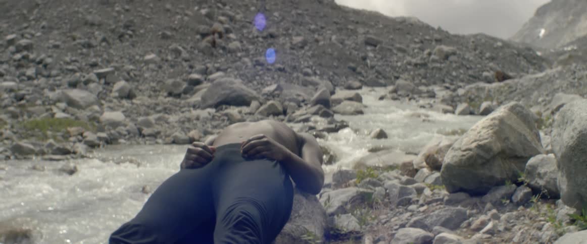 A man is lying back on a rock by the side of a rushing stream