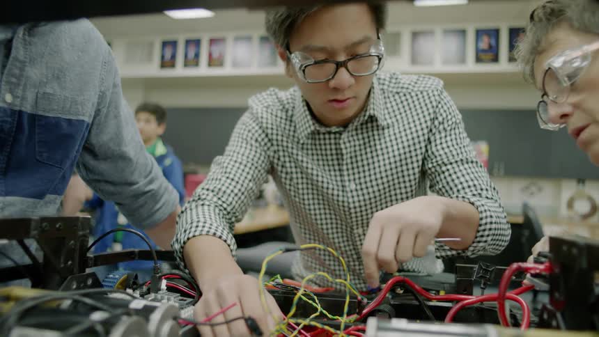 Young men work on electric board in a classroom