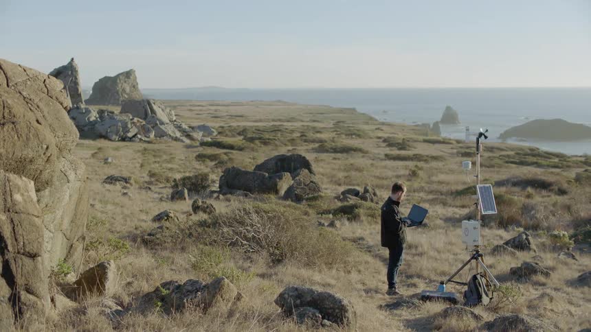 A man stands by a weather monitoring device with a laptop