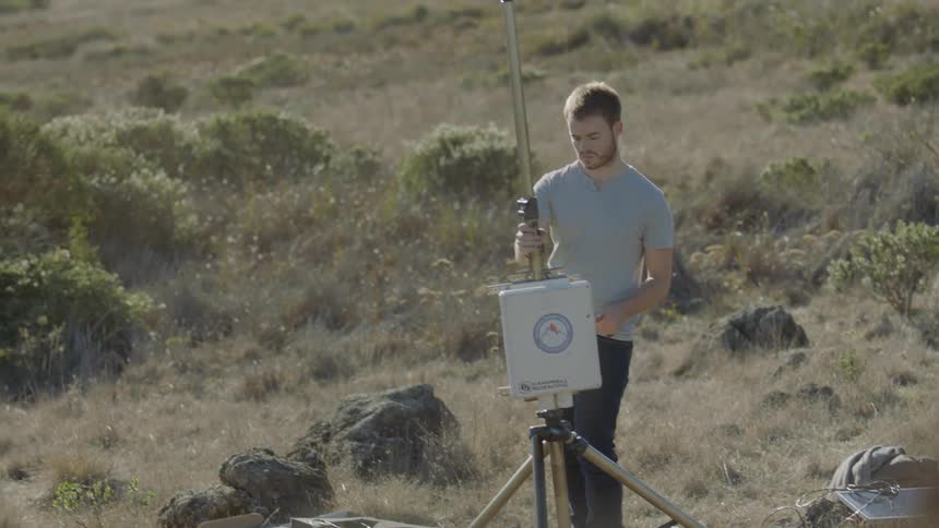 A man sets up weather monitoring equipment on the beach