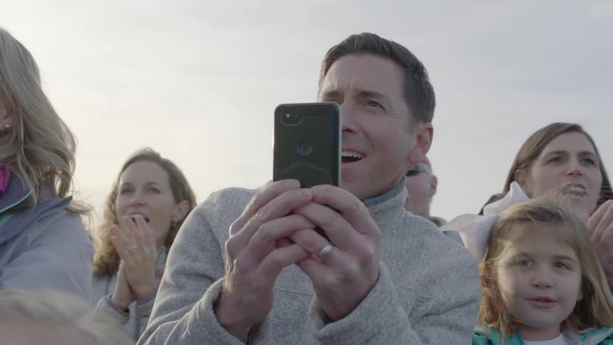 A group of people clap and cheer as a man films with his camera
