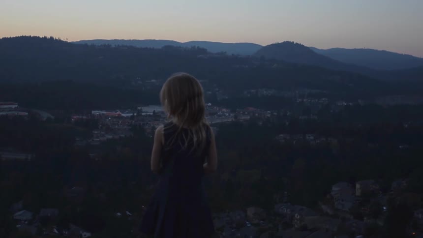 A girl overlooks a mountain range at dusk