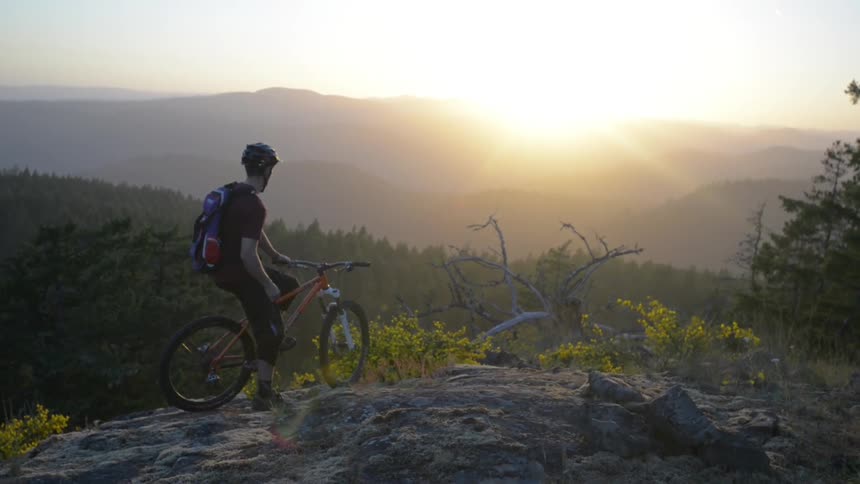 Man sits on his bike on top of a mountain as the sun rises