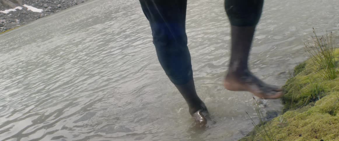 Man walks barefoot through a creek and steps onto shore