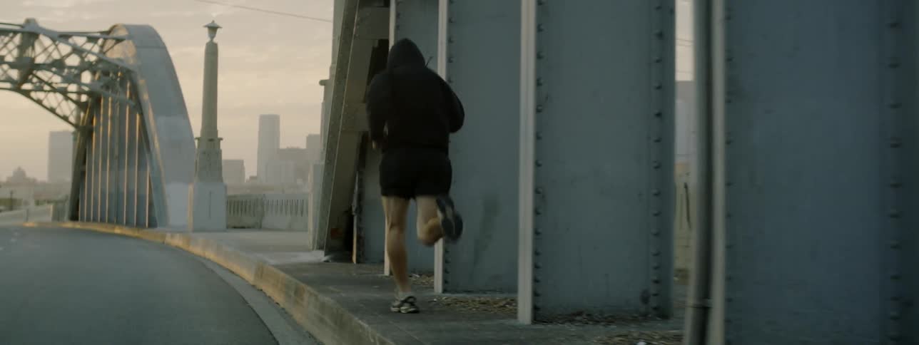 A man is running across a bridge toward a city at dawn