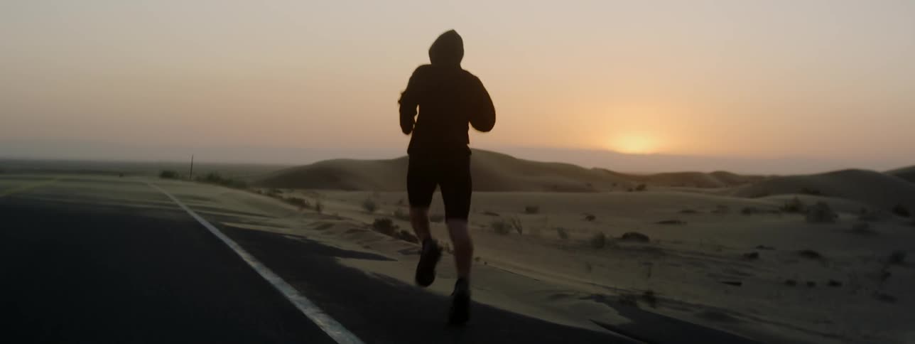 A man is running along the side of the road at sunset