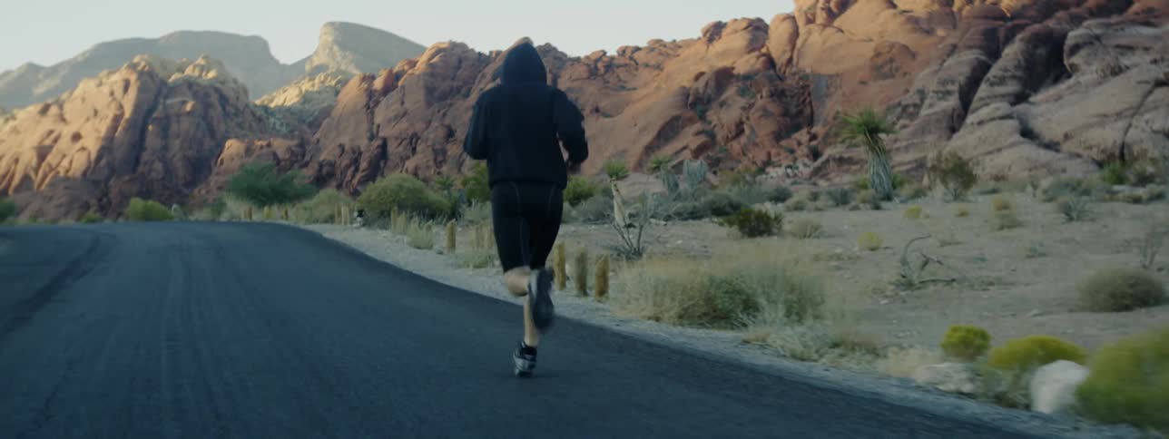 A man is running on the side of a desert highway during the day