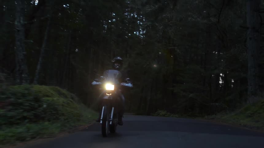 A man rides a motorcycle through a forest in the evening