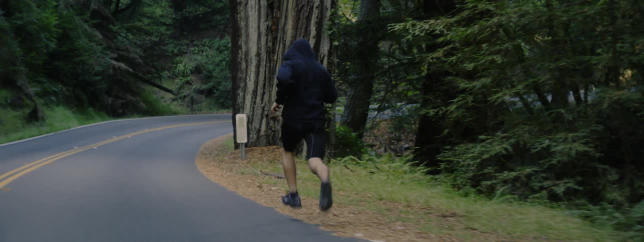 A man jogs down the road near a forest