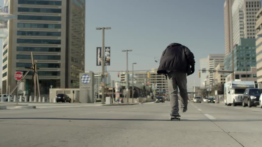 A man does a jump with his skateboard as he rides down a city street during the day