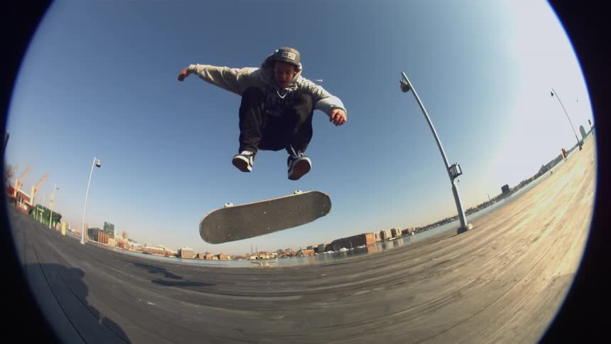 A skateboarder flips his board and lands back on it as he rides on a sunny day