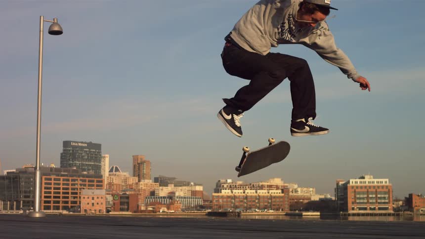 A skateboarder flips his board and lands back on it as he rides on a sunny day