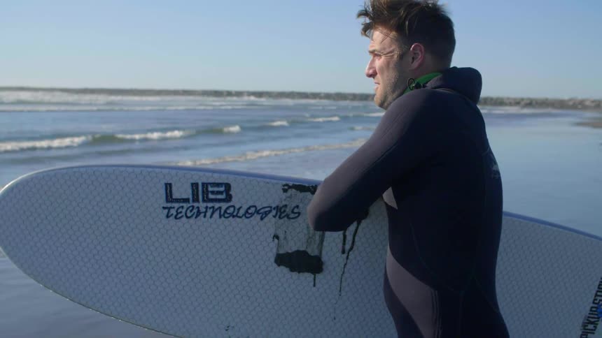 A surfer carries a surfboard on a beach