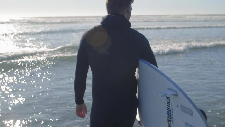Someone is walking through the water carrying a surfboard