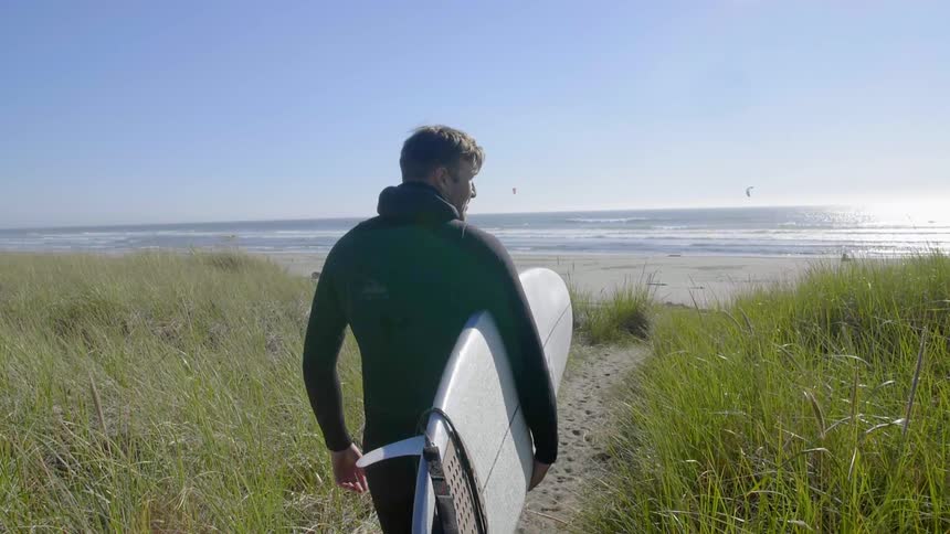 A man is carrying a surfboard to the beach on a sunny day