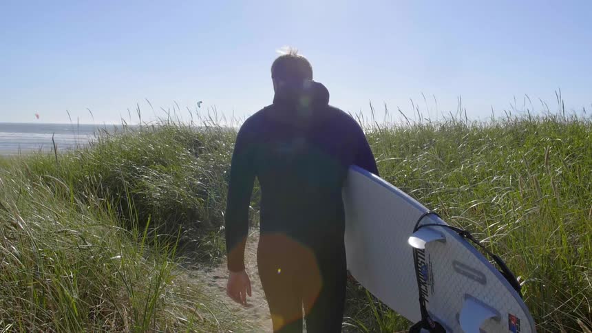 A man is carrying his surfboard to the water on a sunny day