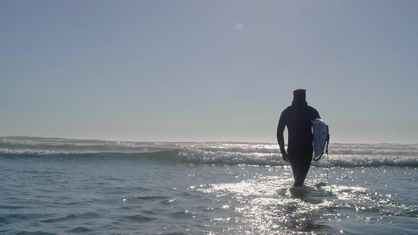 A man holding a surfboard walks into the ocean