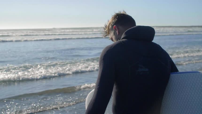 Man holding a surfboard walks towards the ocean