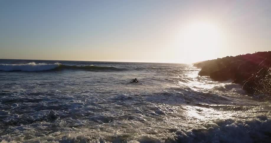 Surfers float on rough waves near the rocky shore