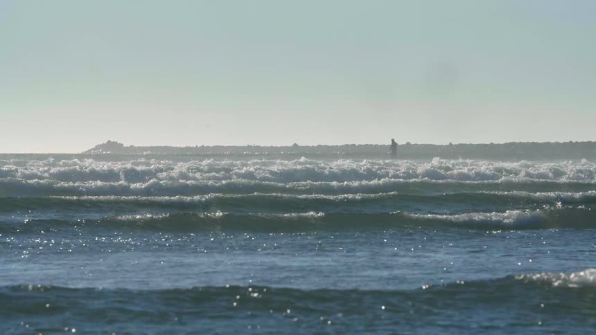 A man on a paddle board is following the waves to shore