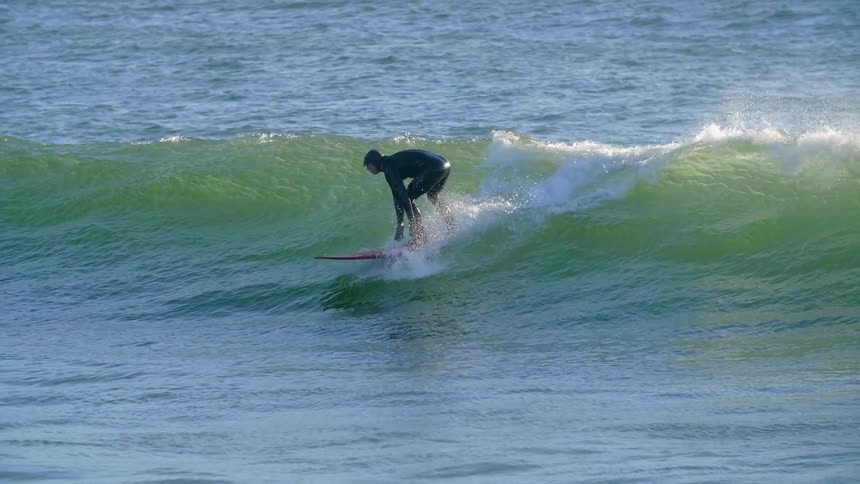A surfer catches a wave on a sunny day
