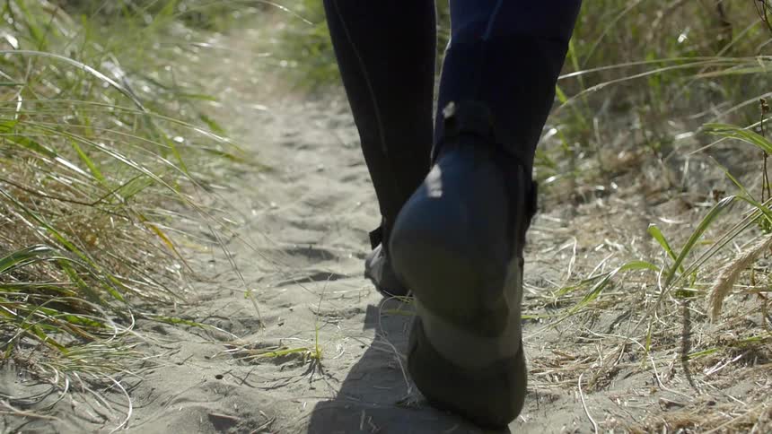 A man in a wetsuit is walking on sand during the day