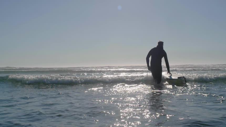 Man carries a surfboard into the ocean