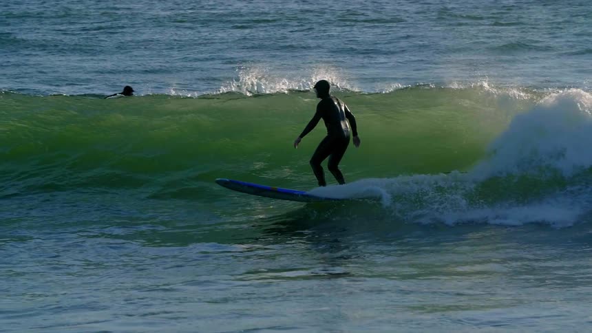 A surfer rides a wave on a sunny day