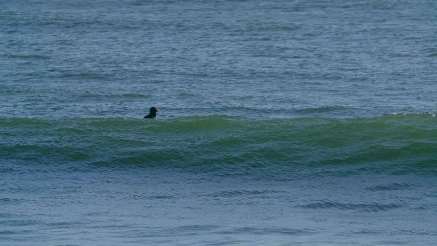 A man is sitting on a surfboard in the ocean awaiting some waves