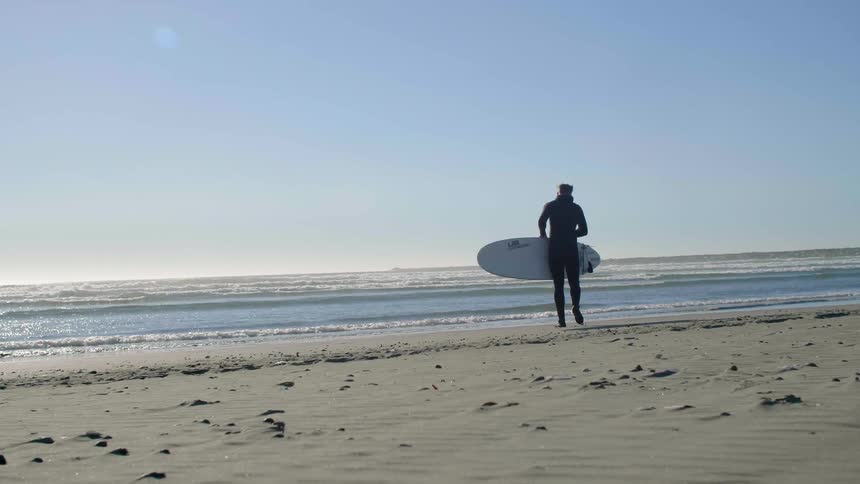 A man is walking with her surfboard towards the ocean