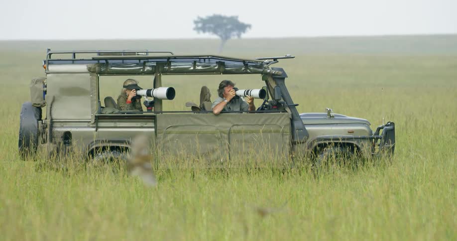 Two people sit in a jeep taking photos with their cameras