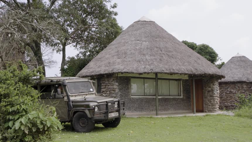 A vehicle pulls up next to a hut in a village