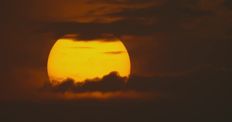 The sun shines bright orange as clouds cross