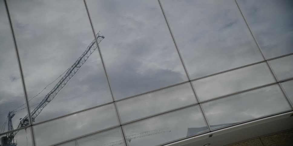 Clouds and construction cranes are reflected in a glass building