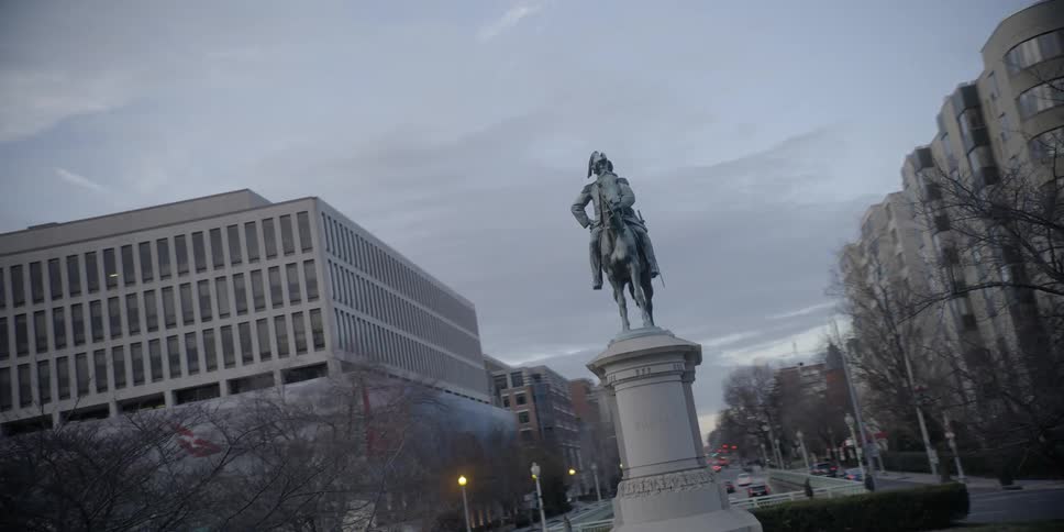 Dusk is falling on a city block with a statue of a general