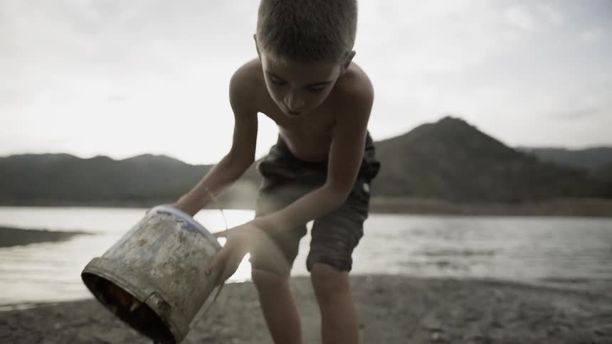 A boy is playing with a bucket on a beach during the day