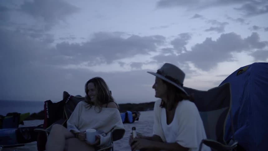 Two women laugh while camping on a beach