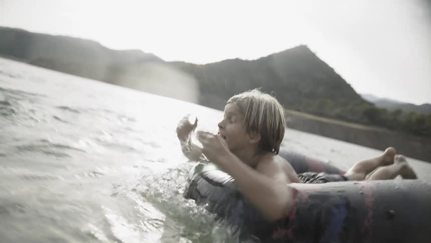 Boy paddling through water while lying on an inner tube at sunset