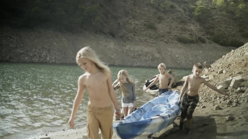 Children carry a canoe along a river's edge