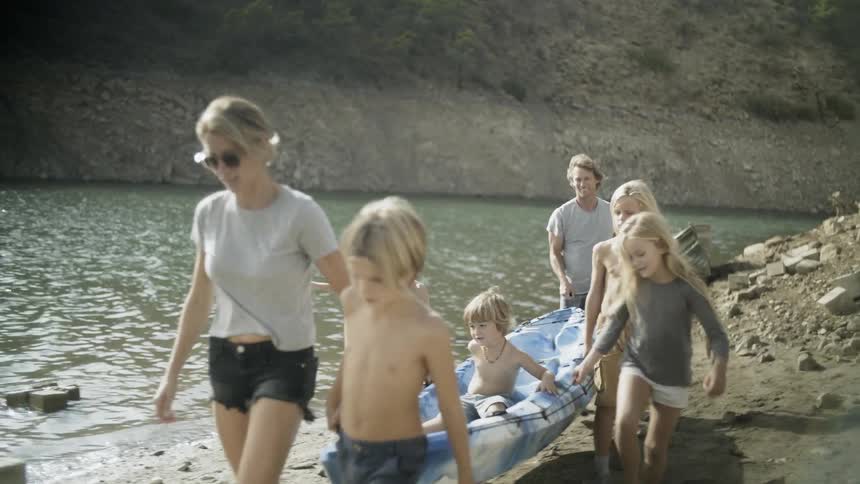 Family carries a kayak next to a lake