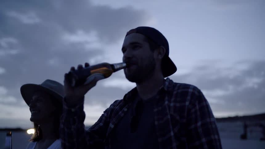 A man and woman drink beer at night by the water