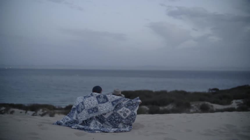 People share a blanket on a sandy beach
