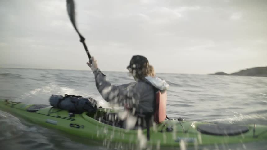 A man is paddling a canoe out into the ocean