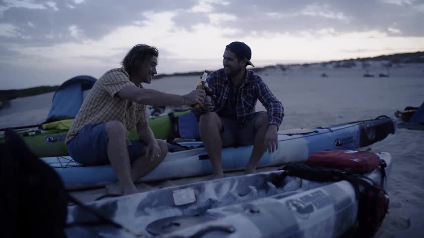 Two guys are sitting on their canoes drinking beer
