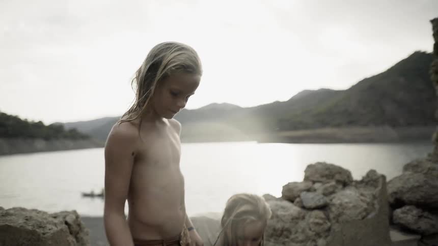 Two kids play near a lake