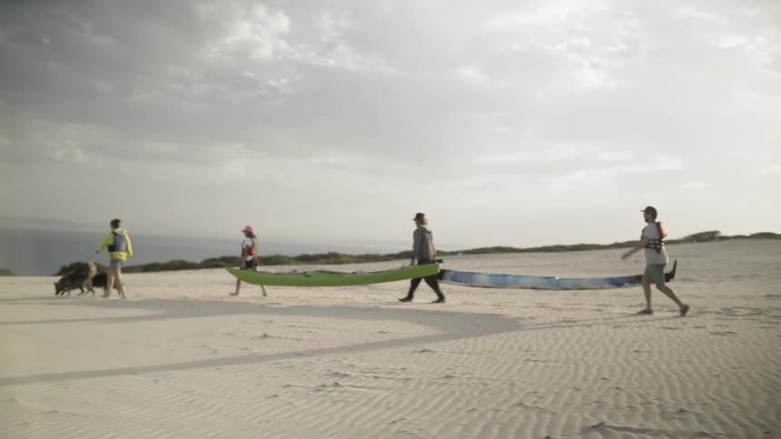 People carry canoes on a sandy beach
