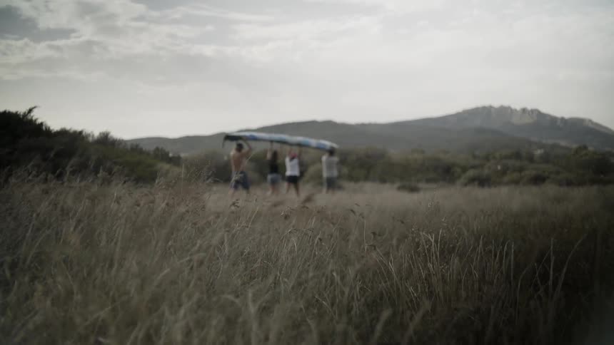 Four friends hold a canoe above their heads as they walk on a trail during the day