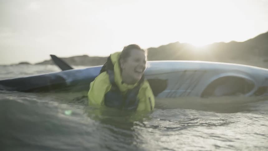 A woman is laughing as her kayak over turns in the ocean