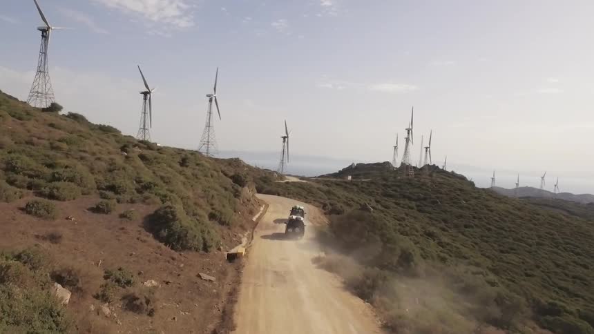 Two trucks drive up a trail towards windmills